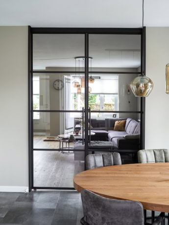 Modern stalen schuifdeur met zwart frame tussen woon-en eethoek.