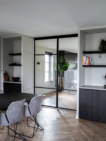 Glazen stalen scheidingswand met zwarte metalen kader, moderne interieur decoratie, scheiding tussen eetkamer en woonkamer, maatwerk stalen deur, stijlvolle woninginrichting.