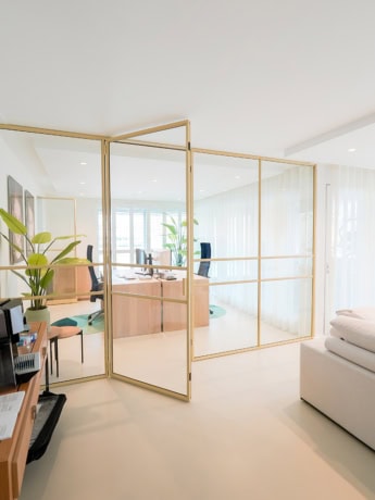 Glas scheidingswand met stalen kaders tussen kantoorruimtes, modern en transparant ontwerp voor een open werkplek.