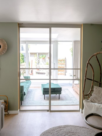 Glastable stalen schuifdeur met aluminium profiel in landelijke woonkamer met groen accent muur en houten vloeren.