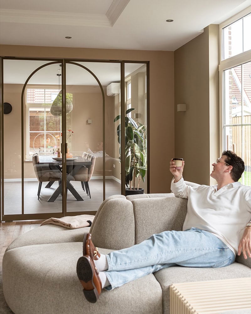 Elegante stalen scheidingsdeur met glazen panelen en zwart frame, gescheiden woon- en eetkamer, natuurlijk lichtinval, moderne binnenhuisarchitectuur.