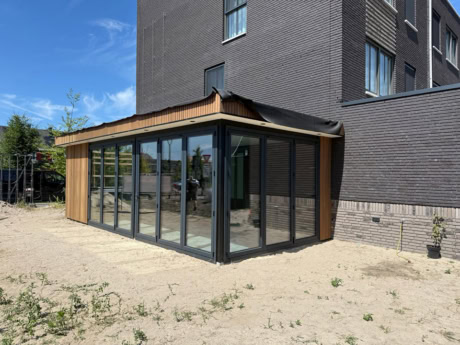 Moderne glazen uitbouw met stalen kozijnen en houten details, perfect voor extra woonruimte of kantoor aan huis, ontworpen door Aluwdoors.