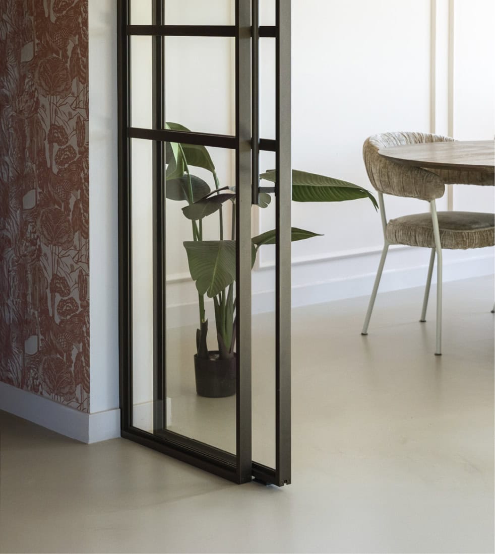 Stalen schuifdeur met glazen panelen in een modern interieur, perfect voor op maat gemaakte wand- en deuroplossingen.