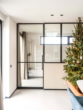 Glass steel sliding door with black frame in modern interior, finished with Christmas tree and decorations for a stylish and festive look, custom steel doors and walls.