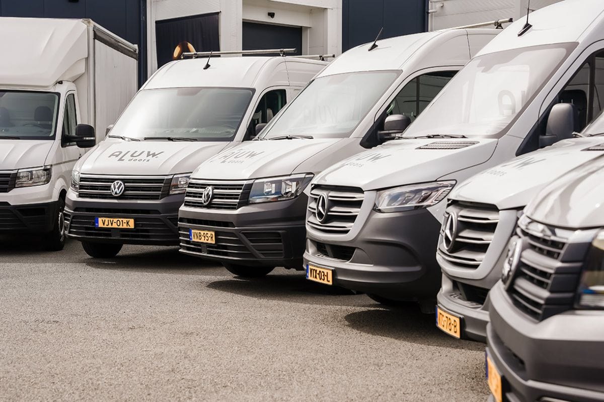 Verschillende bedrijfswagens geparkeerd voor Aluwdoors, gespecialiseerd in maatwerk stalen deuren en wanden.