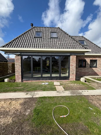 Moderne stalen schuifdeur in een huis met een tuin, grote glazen panelen en een brick gevel, perfect voor een strakke en eigentijdse uitstraling.