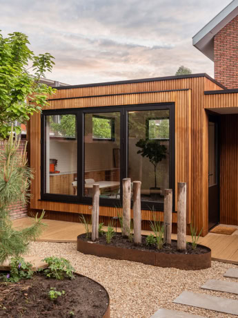 Moderne houten tuinkantoor met grote glazen ramen, omgeven door groen en een tuinpad, perfect voor thuiswerken met een stijlvolle en functionele uitstraling.
