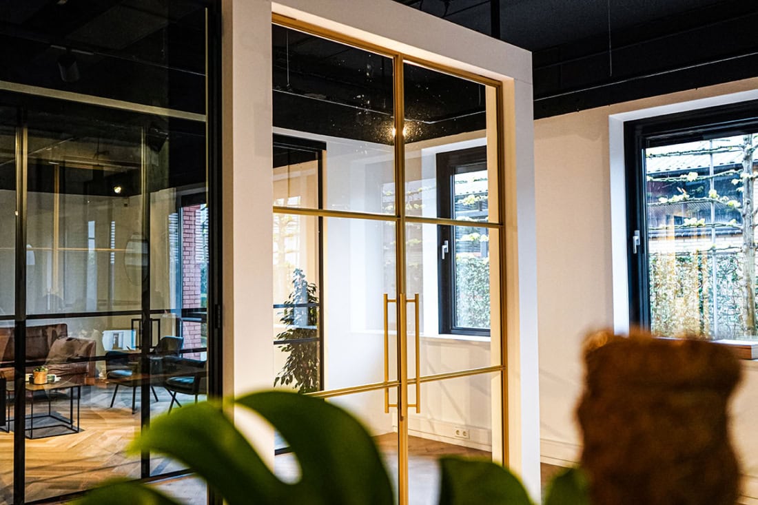Elegante stalen deur met gouden afwerking en glasscheiben, op maat gemaakt voor moderne interieurs en kantoorruimtes.