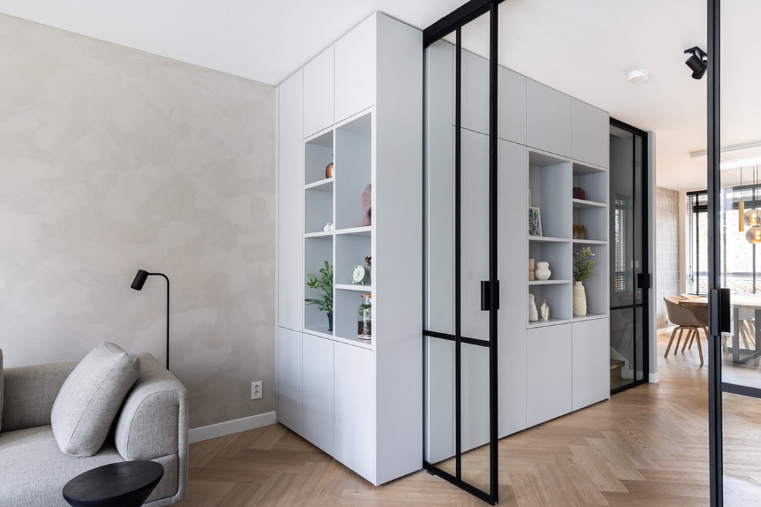 Moderne stalen scheidingswand met glazen deuren en maatwerk indeling, scheidt woon- en eethoek in een eigentijds interieur.