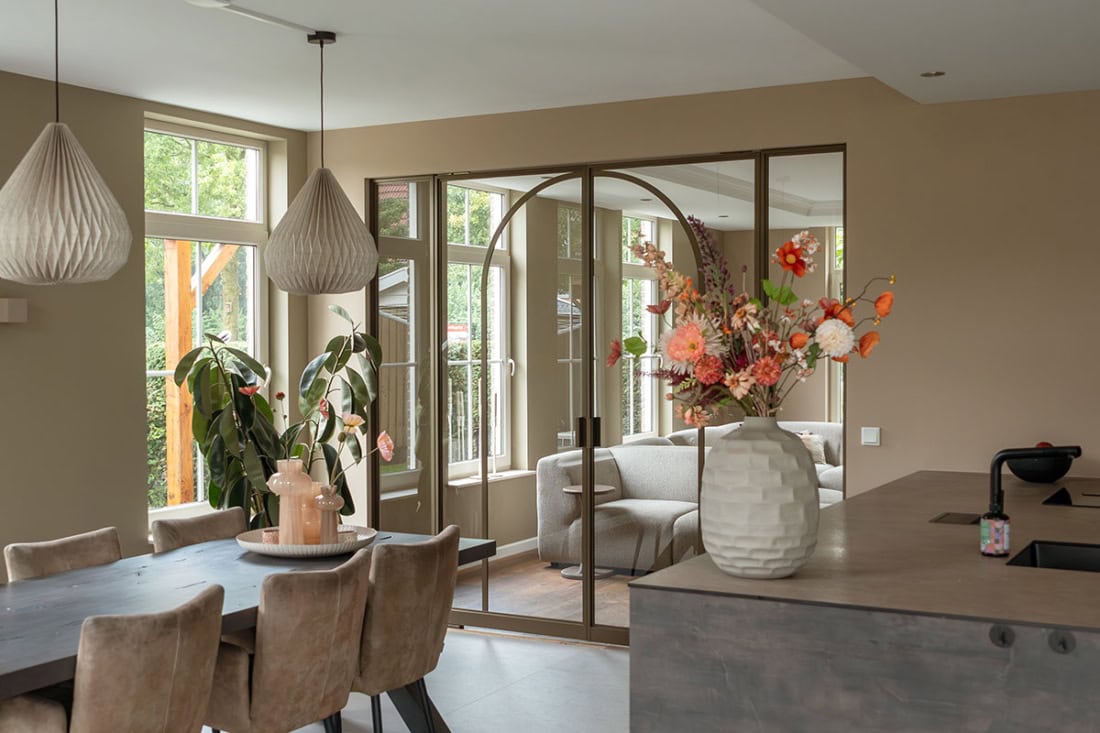 Grote stalen u-style deur met glazen panelen die een moderne scheiding vormt tussen woonkamer en zithoek, op maat gemaakt door Aluwdoors.