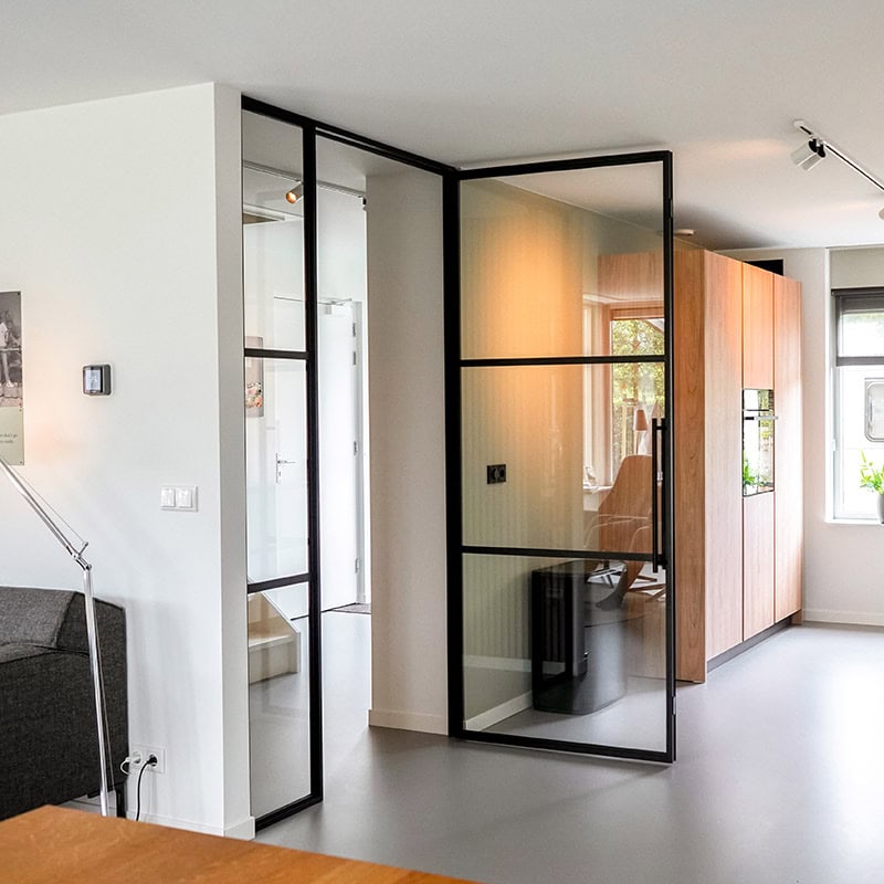 Glazen stalen scheidingswand met zwart metalen frame in modern interieur.