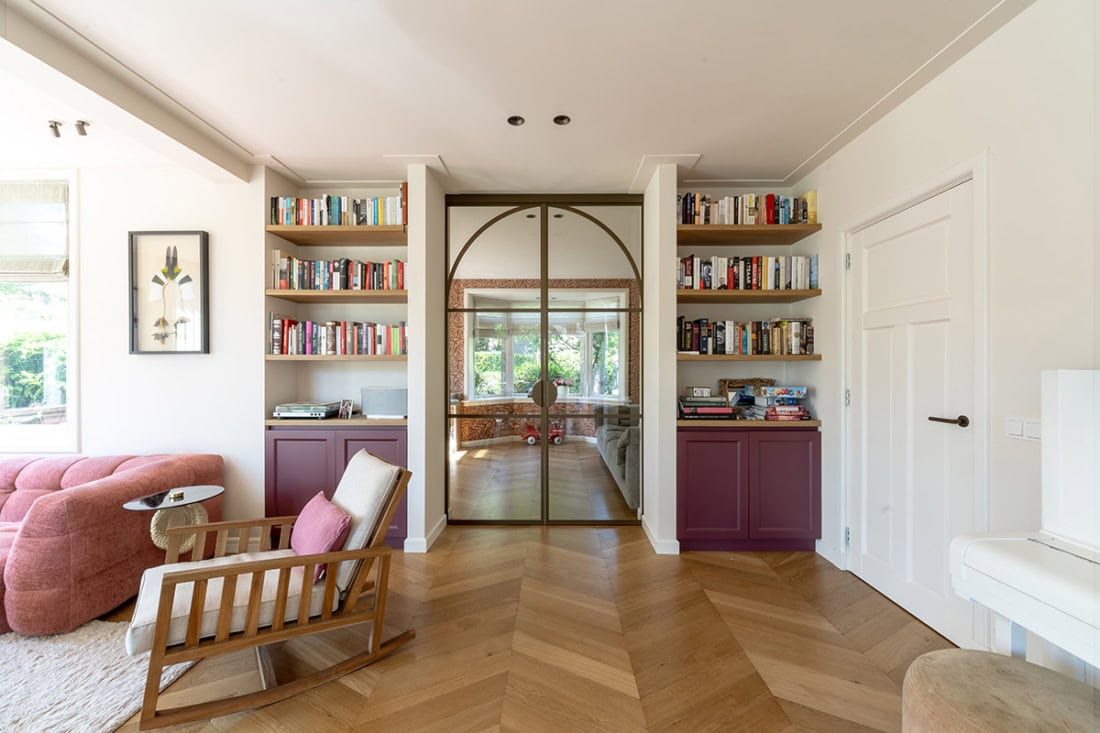 Hoogwaardige stalen schuifdeur met glazen panelen in een moderne woonkamer, inclusief boekenkasten en natuurlijke lichtinval, op maat gemaakt door Aluwdoors.