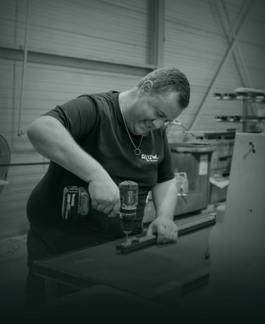 Robuuste man die een stalen deur of wand installeert met een waterpas en een draadloze boormachine in een werkplaats.