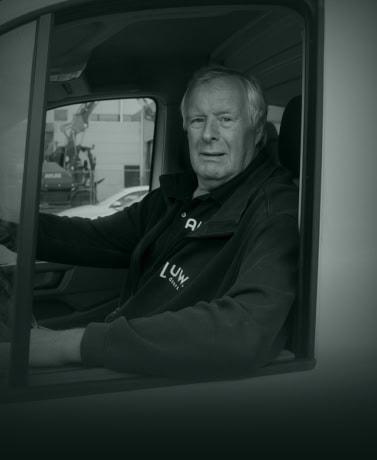 Robuuste man in werkuniform zit in de bestuurdersstoel van een bedrijfswagen, klaar voor levering of installatie van stalen deuren op maat bij Aluwdoors.