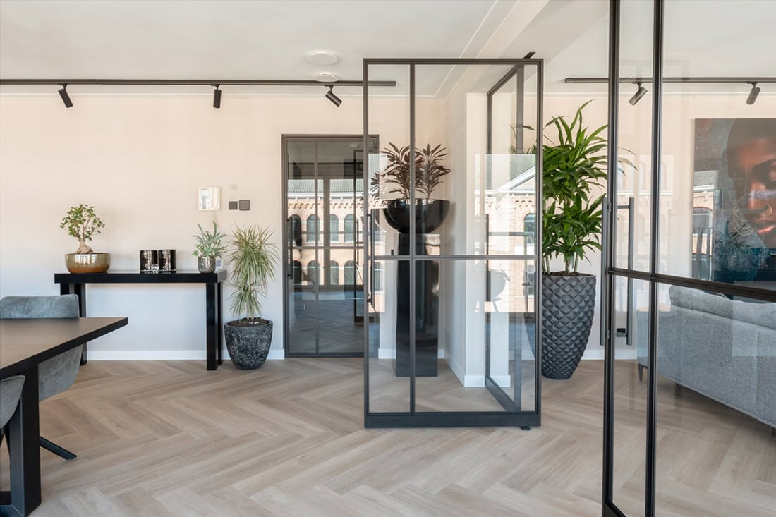 Strakke stalen scheidingswanden en deuren in modern interieur met natuurlijke houtlook vloer.