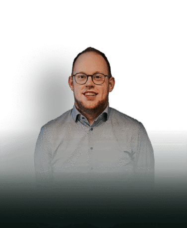 Moderne man in een grijs overhemd en bril, staand voor een zwarte achtergrond, professionele uitstraling, geschikt als vertegenwoordiger of specialist.