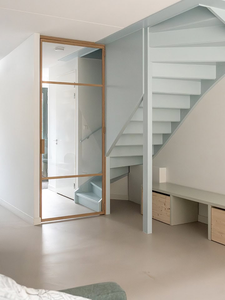 Modern glass dividing door with wooden frame, separates a living room from a staircase and offers an open, bright look in a contemporary interior.