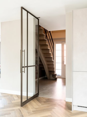 Een stijlvolle combinatie van een houten trap en een stalen deur in een eigentijdse woning, perfect voor een strakke en functionele inrichting.