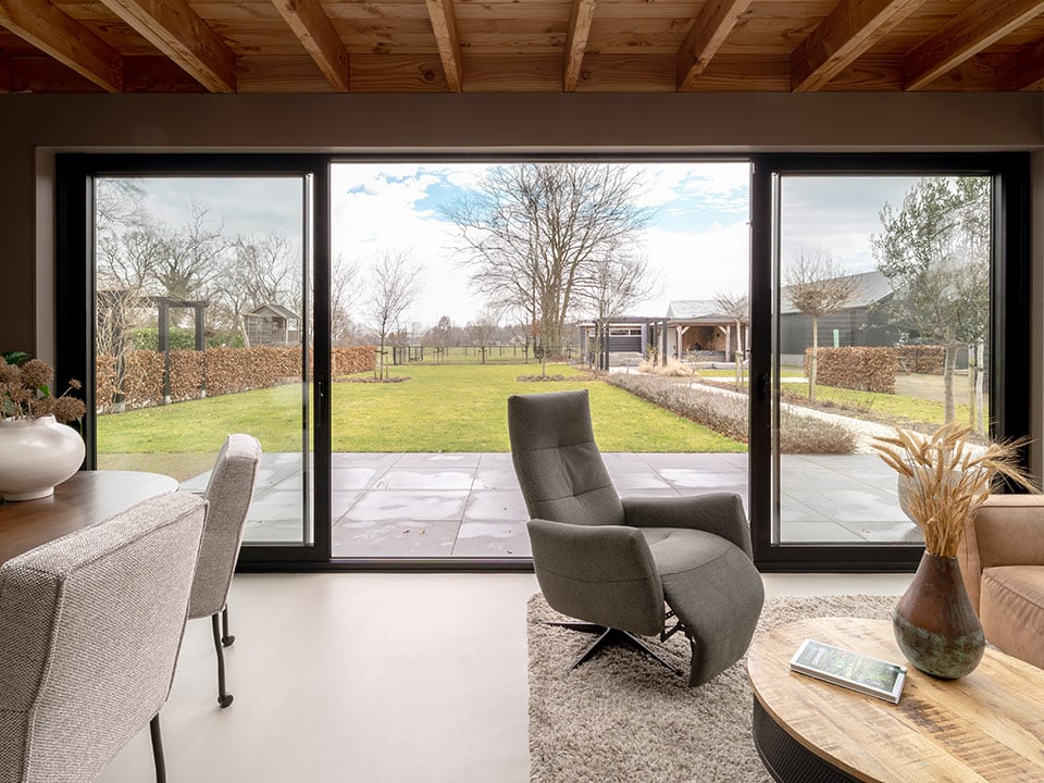 Ruime aluminium buitenpui met grote glazen panelen, ideaal voor een moderne woning in Doornspijk, biedt veel natuurlijk licht en een prachtig uitzicht op de tuin.