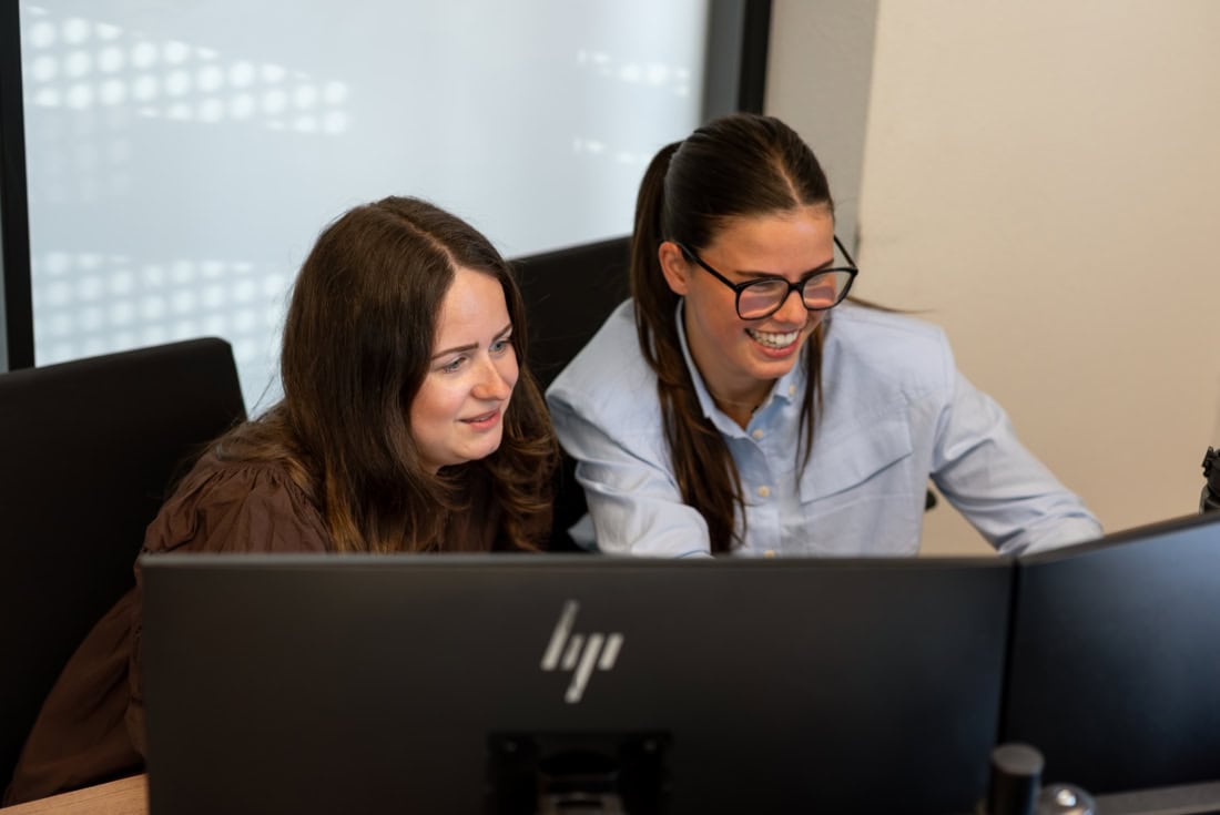 Two women work together on a computer, with a focus on high-quality custom-made steel doors and walls, matching Aluwdoors's services.